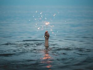 picture of hand emerging from water with fireworks
